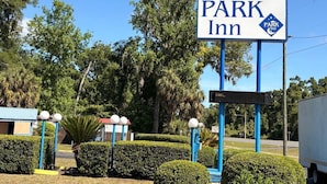 A sign for PARK Inn with a clear view of the surrounding greenery and a building in the background.