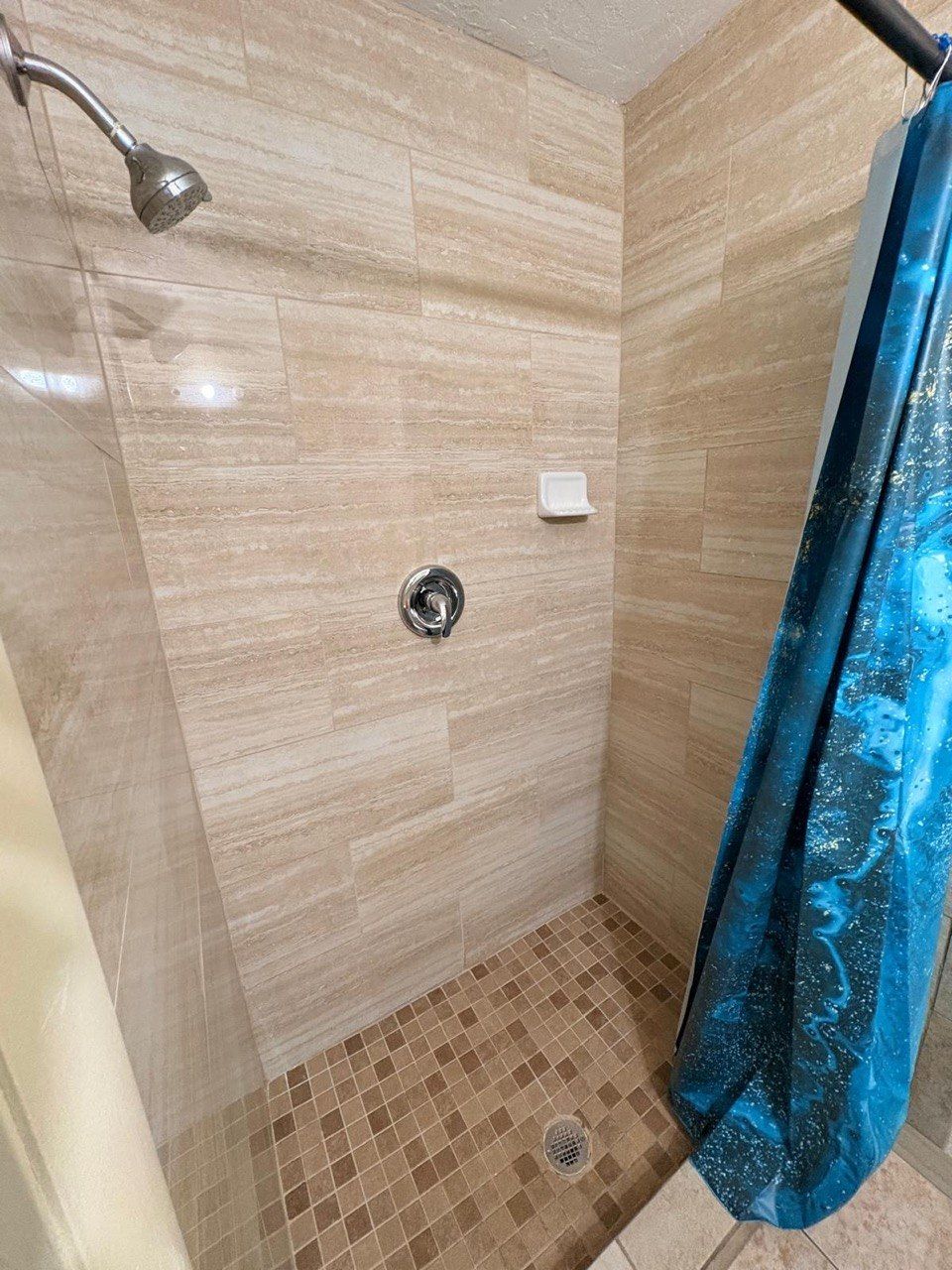 Eine Dusche mit einer verstellbaren Duschbrause, einem Ablaufelement und einem blauen Duschvorhang.