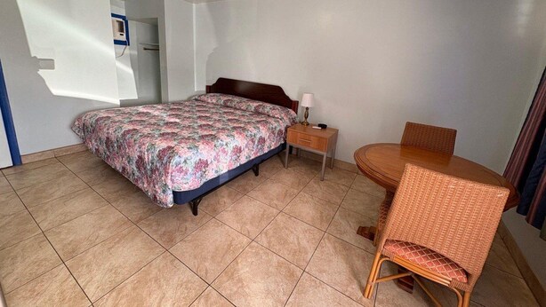 A bedroom with a bed, bedside table, chair, and a small table with a lamp.