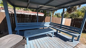 A covered outdoor seating area with a bench and a trash bin.
