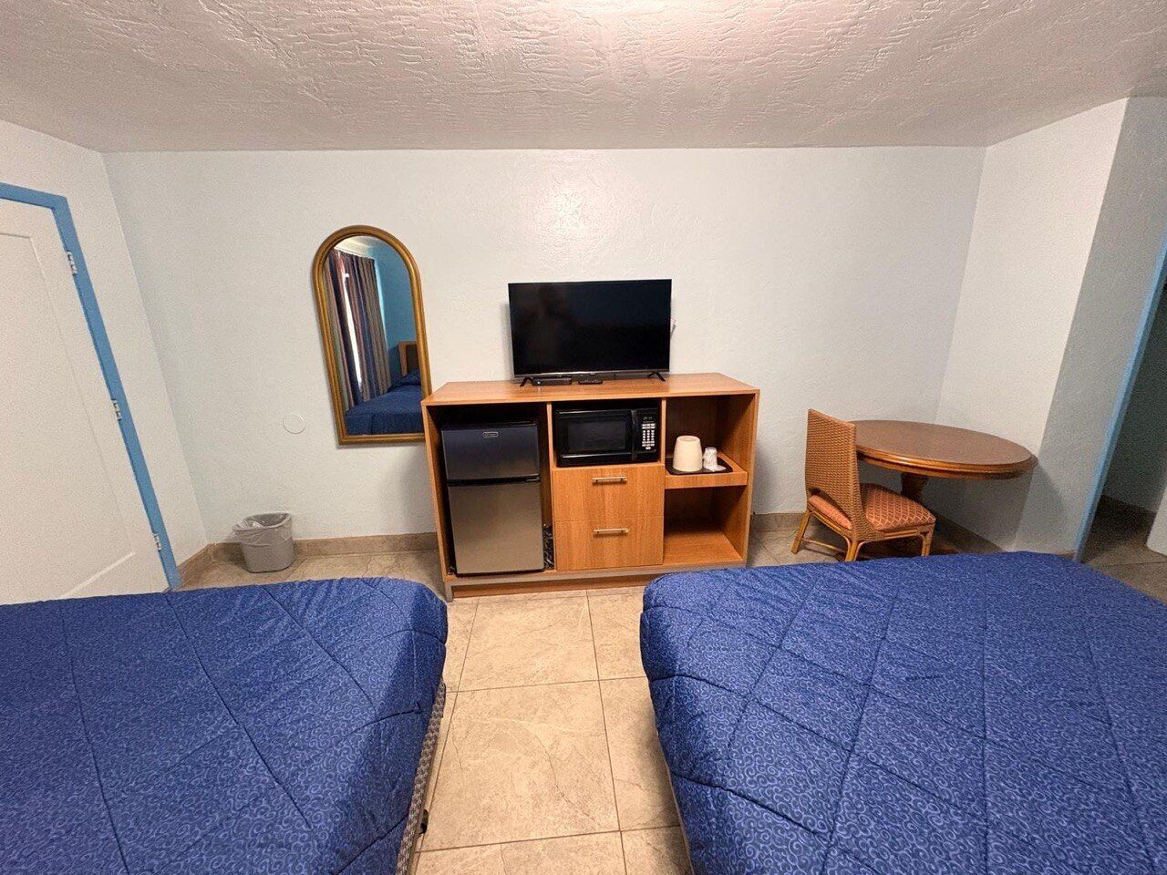 A room with two beds, a small kitchenette, a television, a mirror, and a round table.