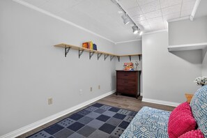 Ein Zimmer mit einem gemusterten Teppich, einer Holzkommode, einem Bücherregal und einem an der Wand befestigten Regal.