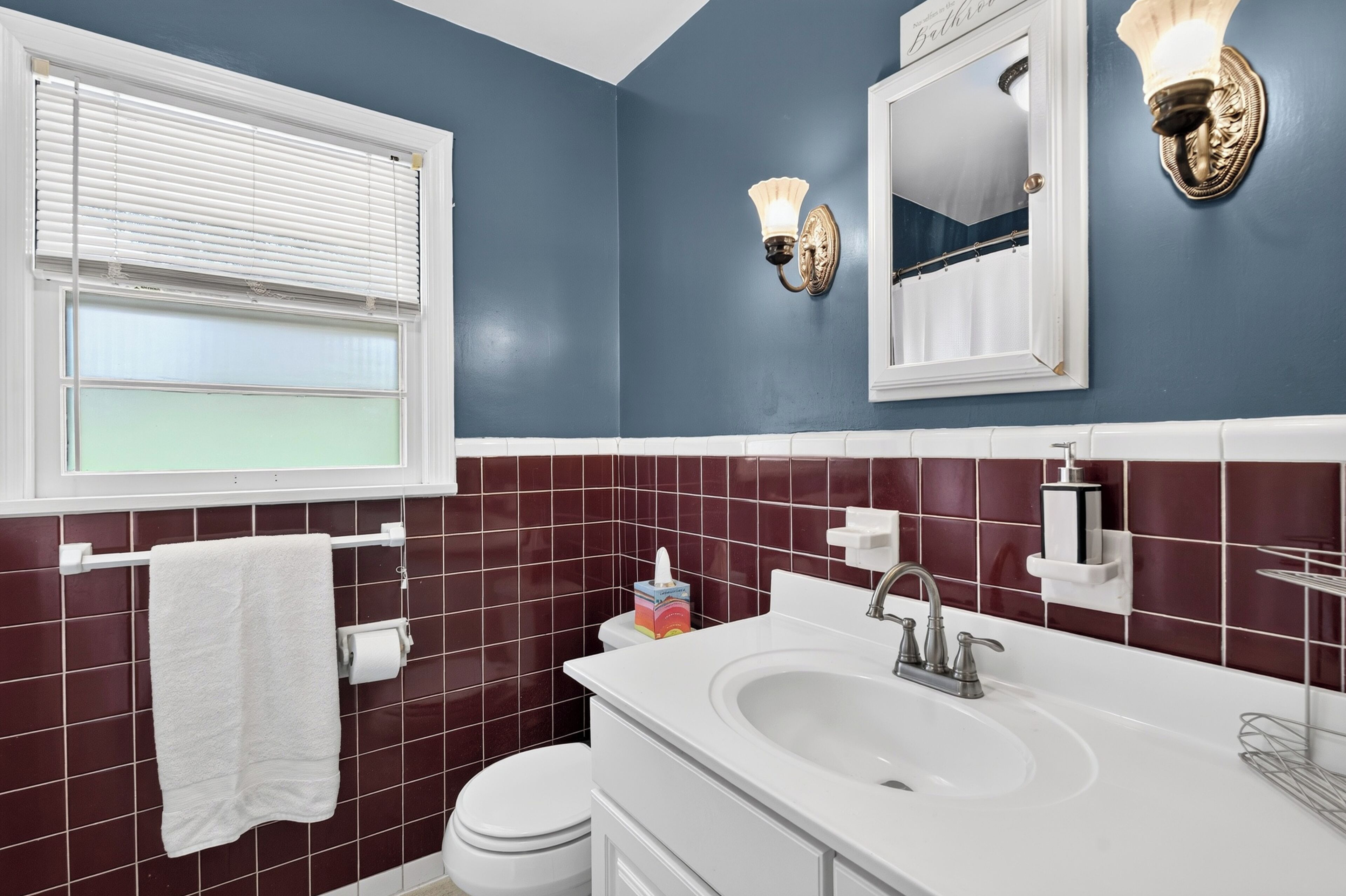 Ein Badezimmer mit einem weißen Waschbecken, einer Toilette und einem Fenster mit Jalousien.
