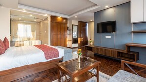 A modern hotel room with a large bed, a TV mounted on the wall, and a seating area with a coffee table. - Apex Business Hotel (Kathmandu)
