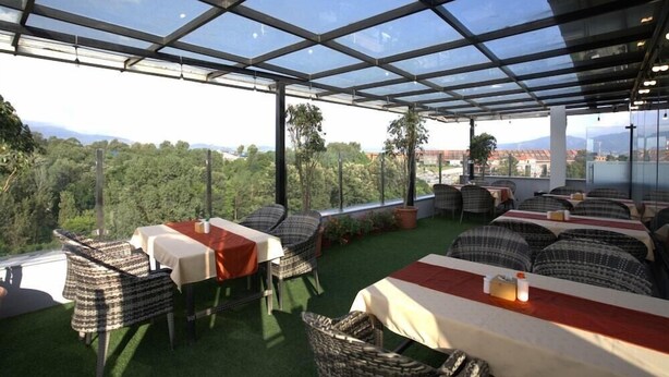 An outdoor dining area with tables and chairs, a glass roof, and a view of the landscape. - Apex Business Hotel (Kathmandu)