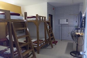 Une chambre avec des lits superposés, une échelle, un bureau, un ventilateur et un appareil de climatisation.