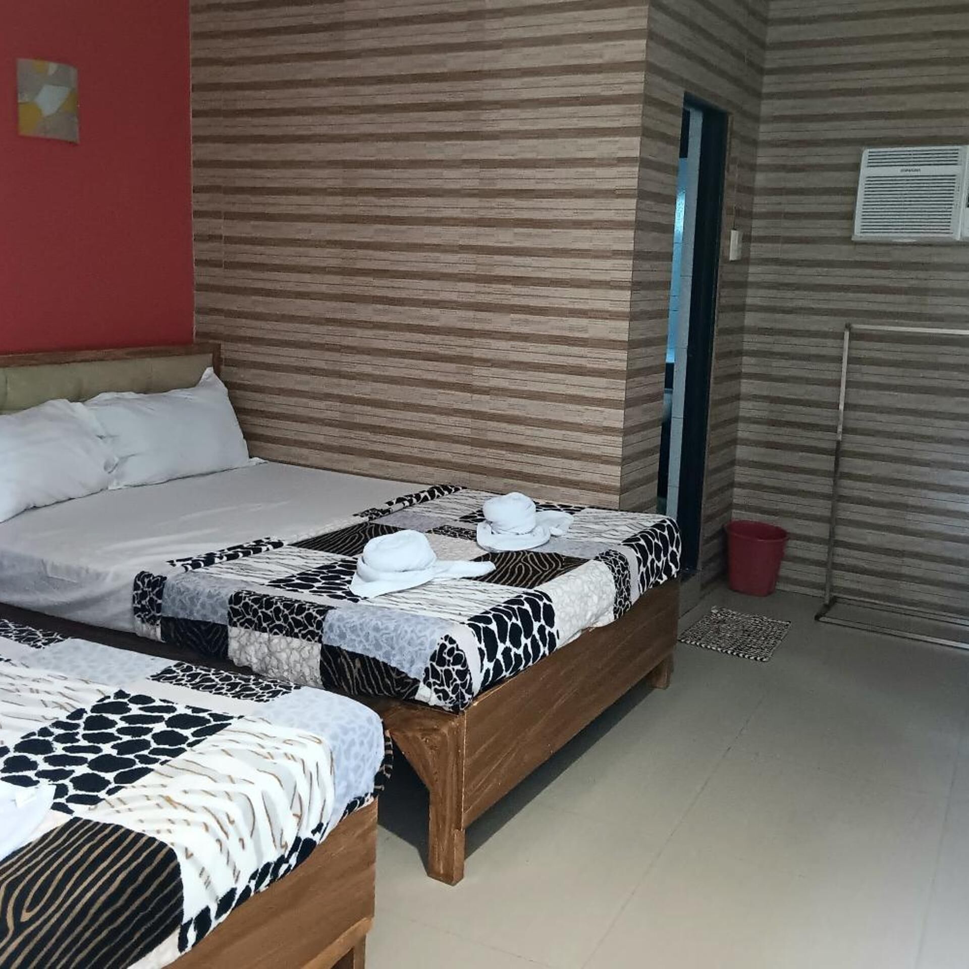 A hotel room with two beds, a red wall, and a patterned floor.