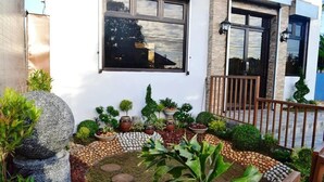 A well-maintained garden with various plants and decorative stones, a wooden fence, and a building with a window and door. - Casa Del Camba Hotel and Restaurant by Zuzu (Alaminos)