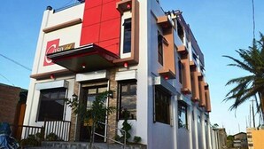 A two-story building with a prominent red section on the upper level, a visible entrance, and a clear sky. - Casa Del Camba Hotel and Restaurant by Zuzu (Alaminos)