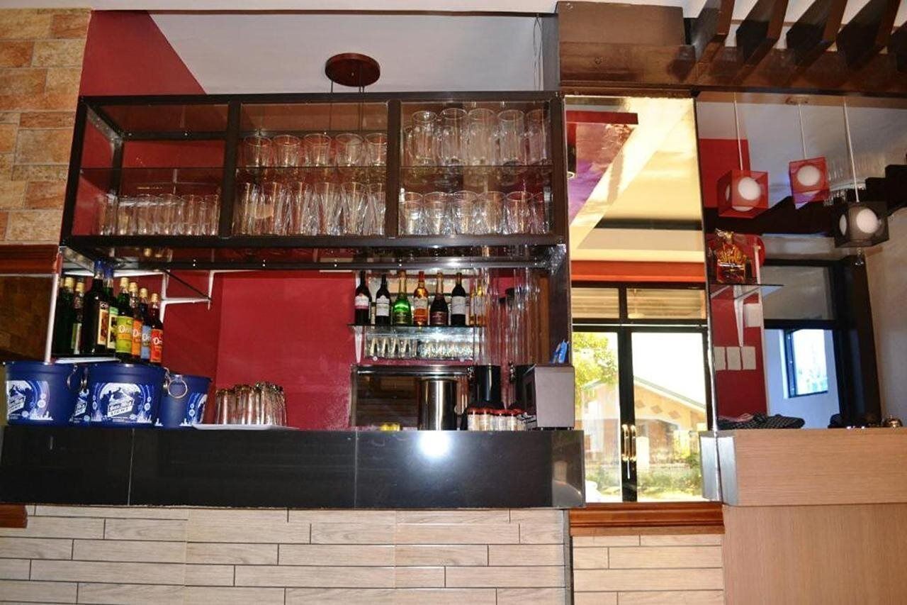 A bar area with shelves of bottles and glasses, a counter, and a view of the outside.
