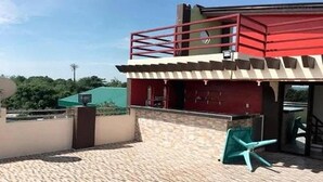 A building with a red and white exterior, a balcony, and a paved patio area with a chair. - Casa Del Camba Hotel and Restaurant by Zuzu (Alaminos)