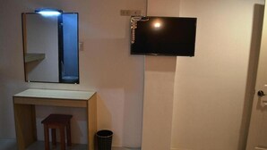 A small bathroom with a mirror, a sink, a stool, a trash can, and a television mounted on the wall. - Casa Del Camba Hotel and Restaurant by Zuzu (Alaminos)