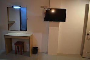 Un baño pequeño con un espejo, un lavamanos, un taburete, un bote de basura y un televisor montado en la pared.