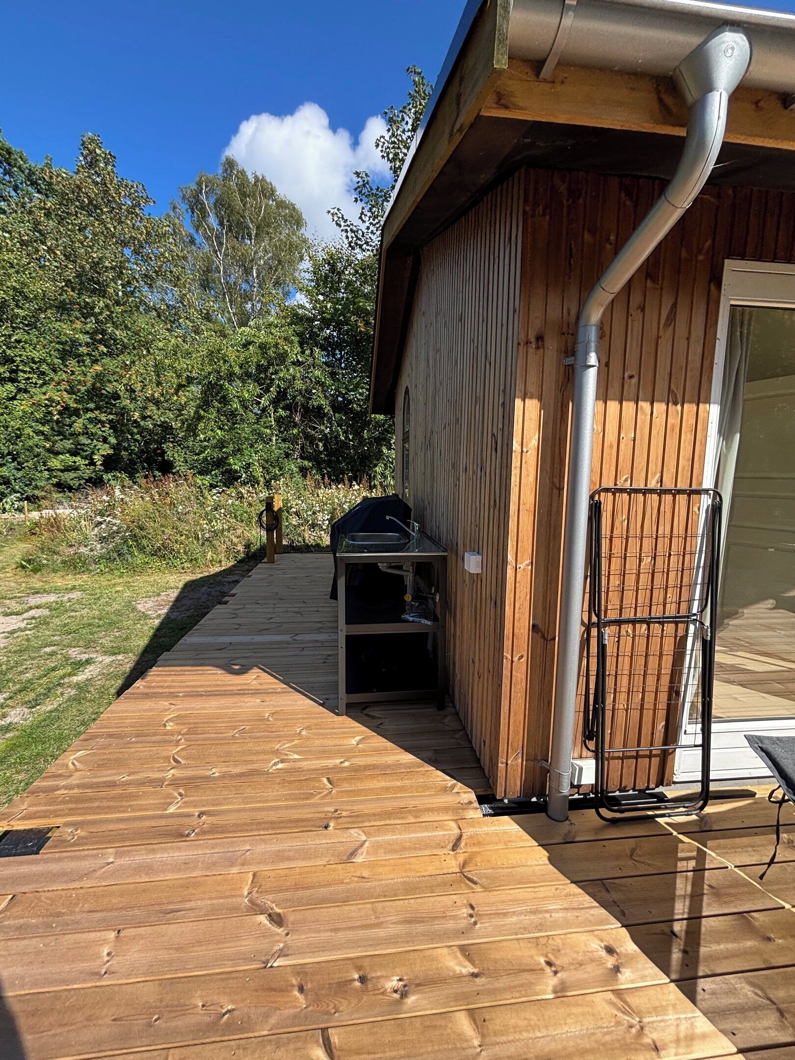 A wooden deck leading to a building with a metal gutter and a grill outside.