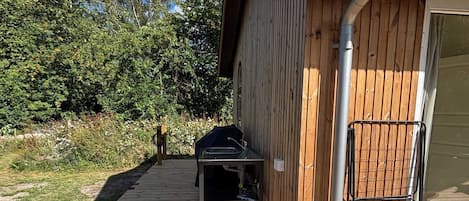 A wooden deck leading to a building with a metal gutter and a grill outside.