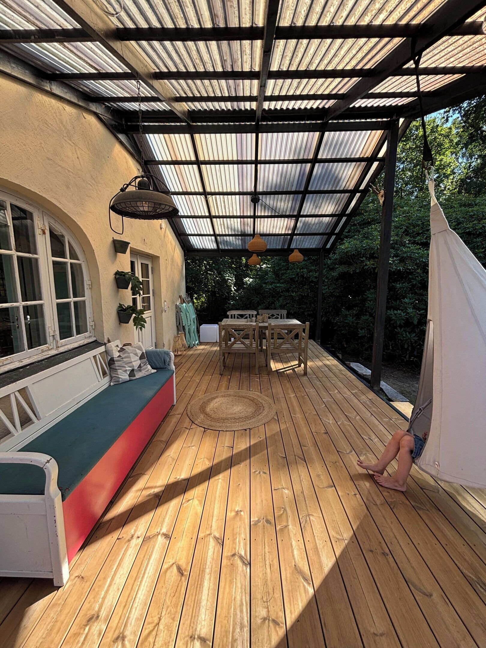 A covered outdoor patio with a wooden deck, a cushioned seating area, and a hammock.