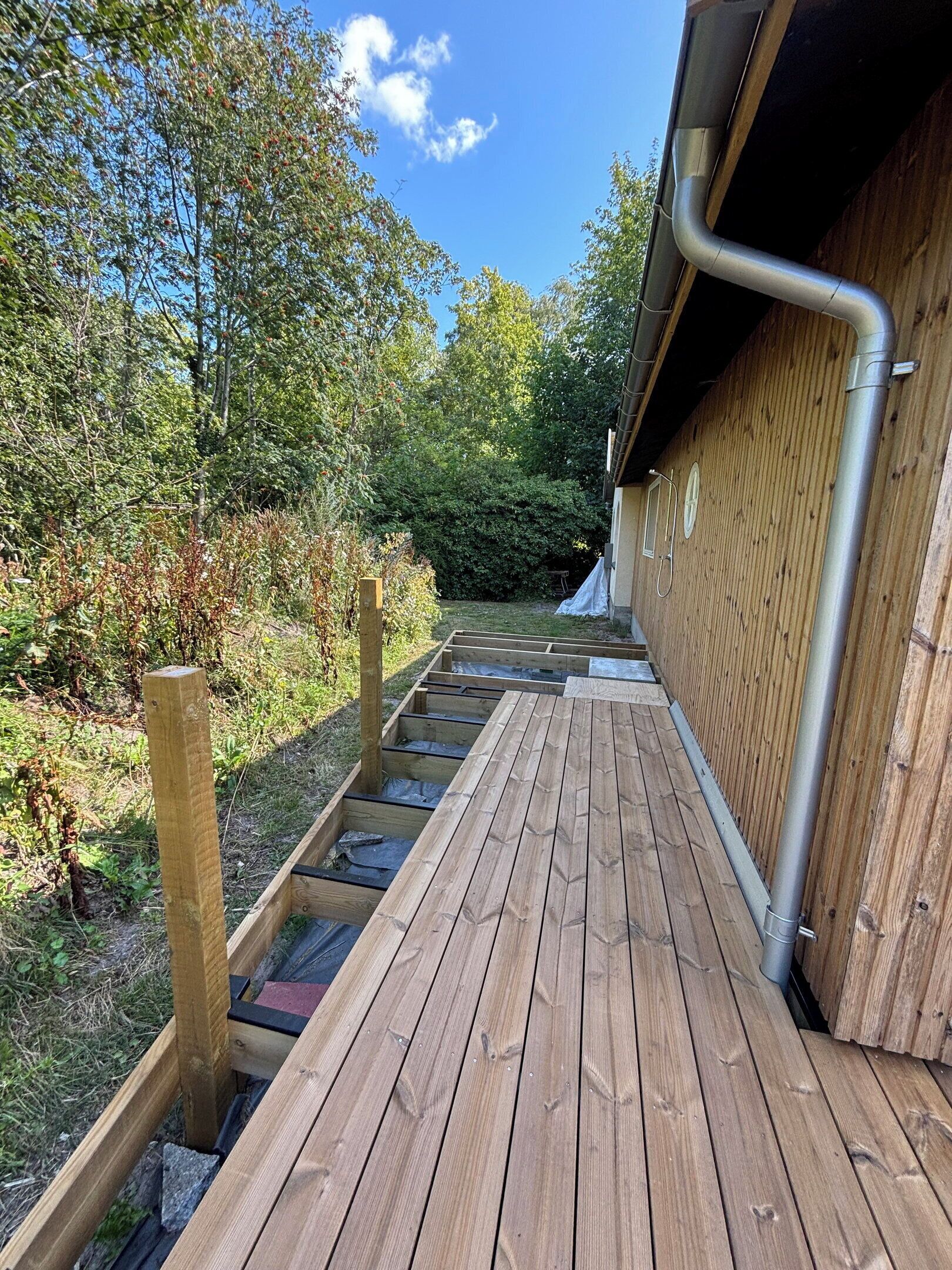 Una terraza de madera que conduce a un edificio con canalón de metal.
