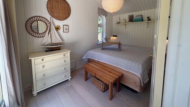 Ein Schlafzimmer mit einem Bett, einem Schminktisch, einer Bank, einer Hängeleuchte und einem Wandspiegel.