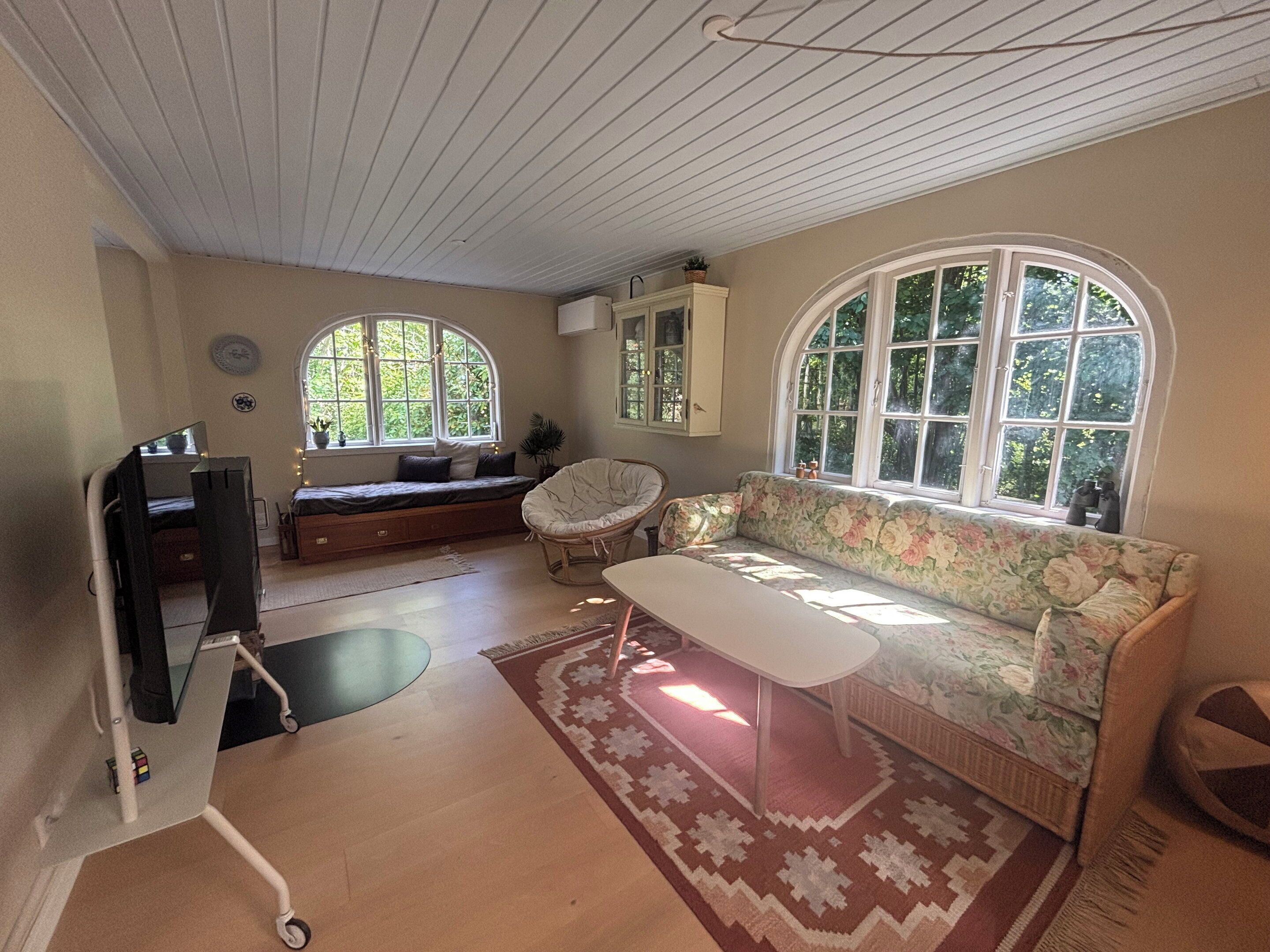 Habitación con sofá, una silla, una mesa y ventana con vista a zonas verdes.