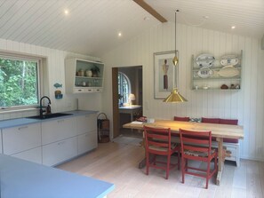 A kitchen with a window, a sink, and a dining area with a table and chairs. - Lovely summer house from 2025 in Rørvig (Nykøbing Sj)