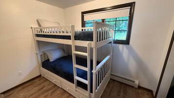 Une chambre avec un lit superposé, une fenêtre, un plancher en bois et un mur blanc.