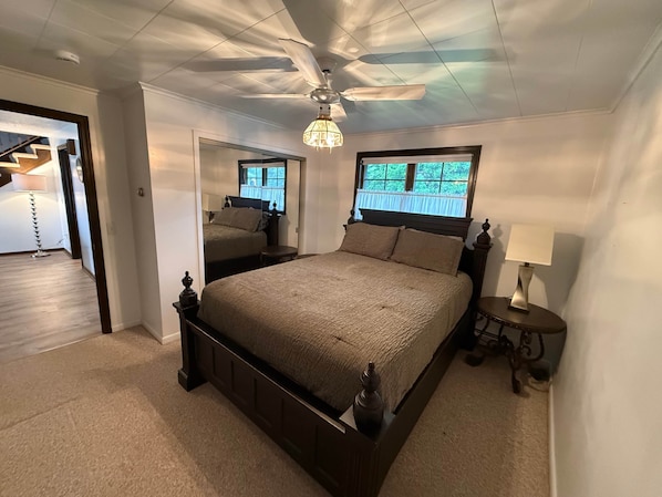 A bedroom with a large bed, a ceiling fan, a window with a view, and a lamp on a bedside table.