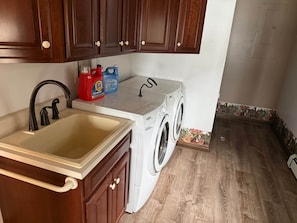 A kitchen with a sink, wooden cabinets, a washing machine, and cleaning supplies.