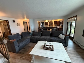 A modern living room with a sectional sofa, a coffee table with decorative items, and a view into the kitchen.