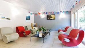 A modern waiting area with comfortable seating, a coffee table with magazines, and a television screen. - Residence Vacanceole Les Chambres de la Baie (Roz-sur-Couesnon)