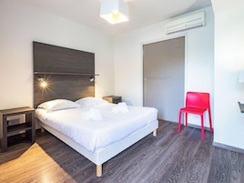 Una habitación de hotel moderna con una cama grande, mesitas de noche, una silla roja y un equipo de aire acondicionado.