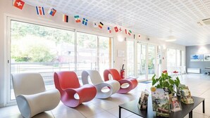 A modern waiting area with colorful chairs, a table with brochures, and a ceiling with patterned tiles. - Residence Vacanceole Les Chambres de la Baie (Roz-sur-Couesnon)