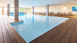 An indoor swimming pool with wooden deck, lounge chairs, and a tiled ceiling. - Residence Vacanceole Les Chambres de la Baie (Roz-sur-Couesnon)