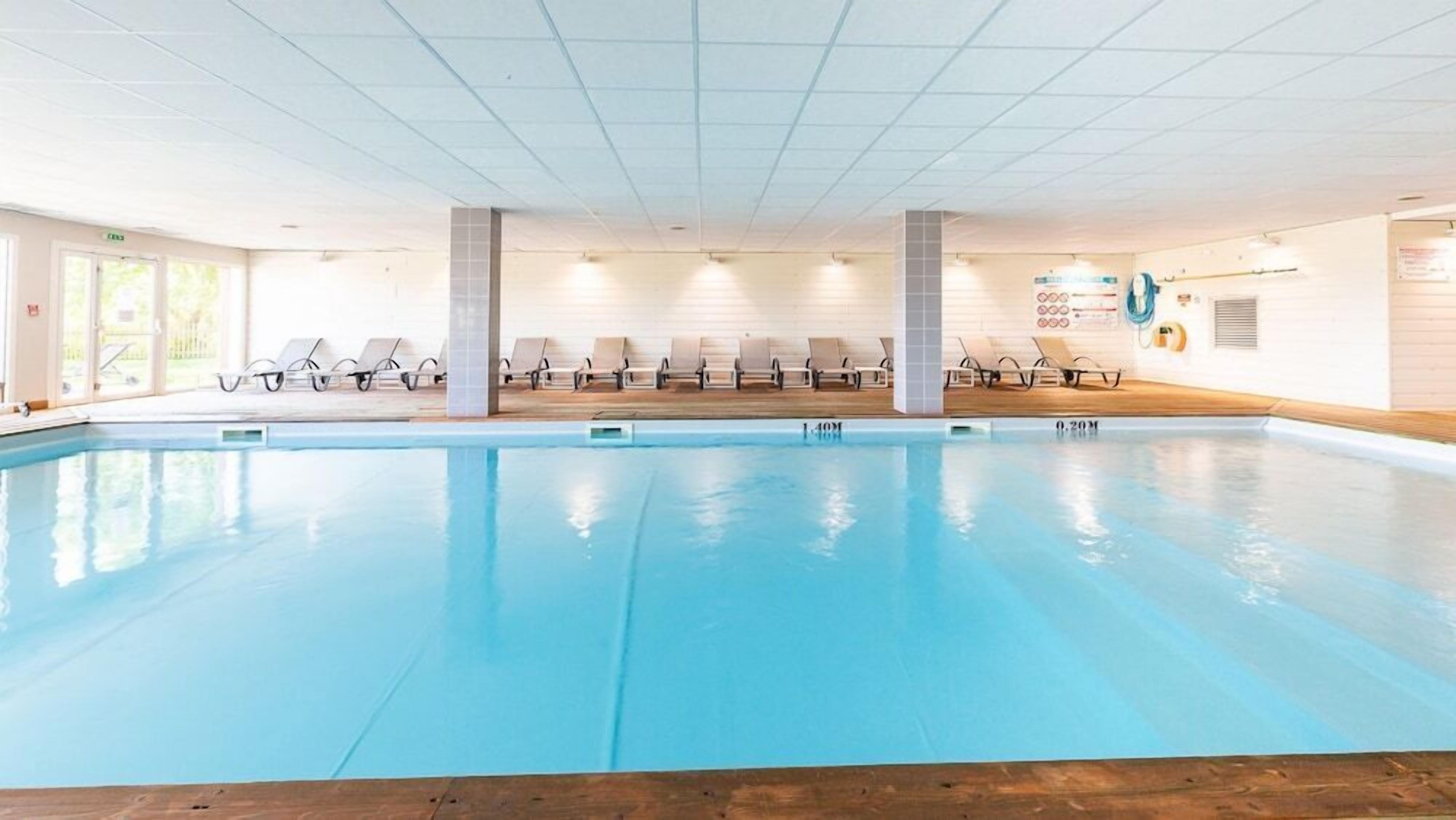 A large indoor swimming pool with multiple lounge chairs and a wooden deck area.