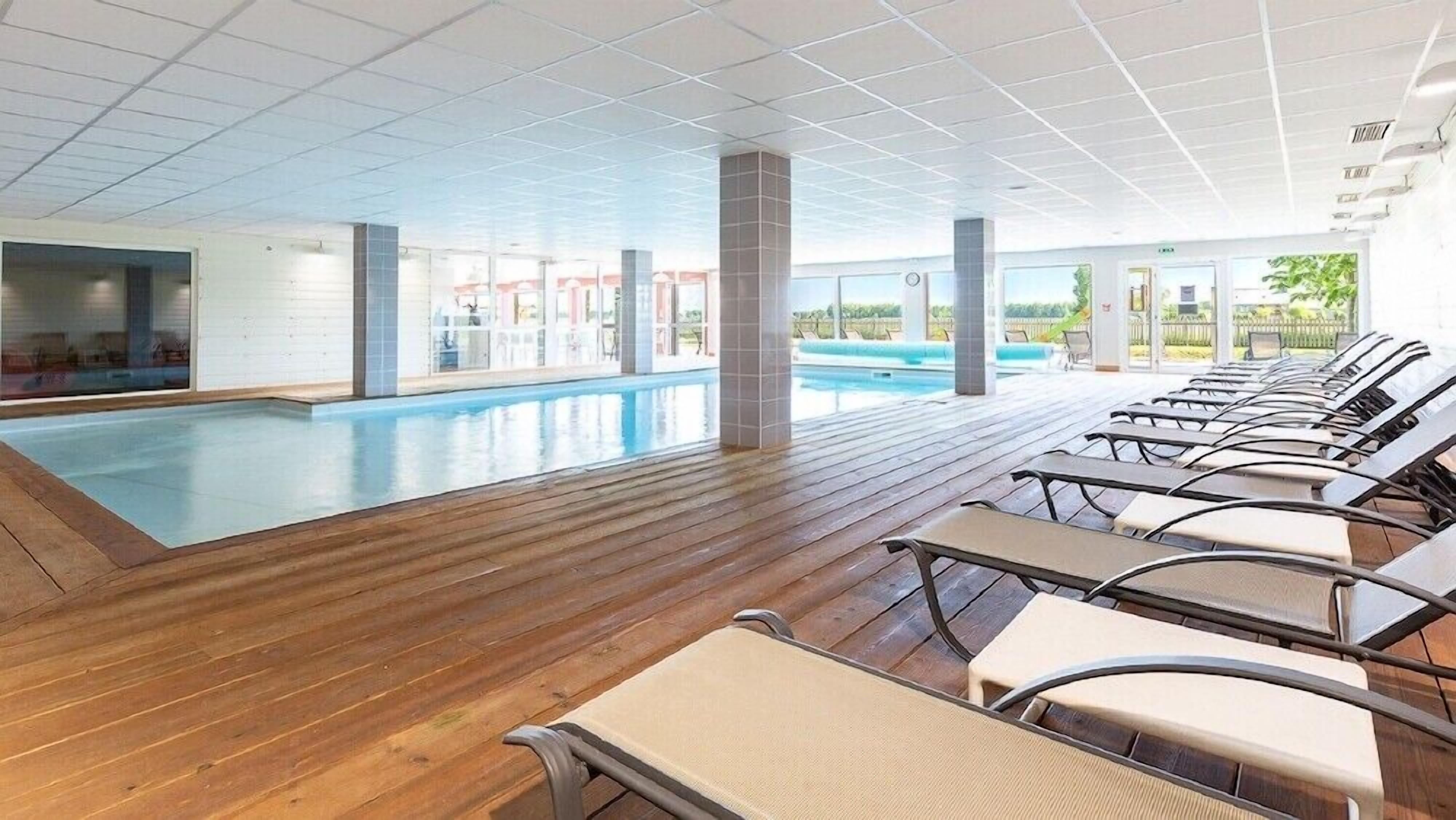 An indoor swimming pool with a wooden deck and lounge chairs.
