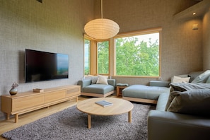 A modern living room with a flat-screen TV, a wooden console, a round coffee table, and two sofas. - Ume House (Kutchan)