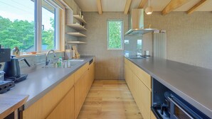 Et moderne køkken med træskabe, en stålbordplade og et vindue med udsigt til grønne omgivelser.