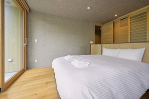 A hotel room with a large bed, a wooden floor, a textured wall, and a ceiling with recessed lighting. - Ume House (Kutchan)