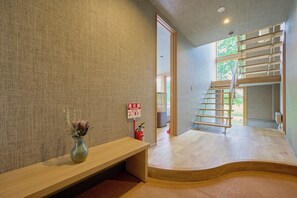 A modern interior with a wooden bench, a fire extinguisher, and a staircase leading to an outdoor area. - Ume House (Kutchan)