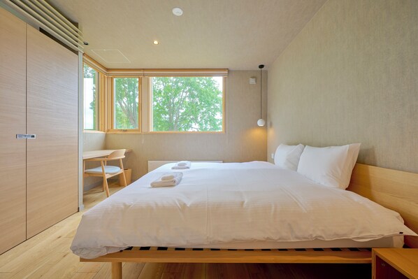 A bedroom with a large bed, a desk, and a window with a view of trees. - Ume House (Kutchan)