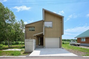 A modern two-story house with a garage, a concrete block, and a truck parked outside. - Ume House (Kutchan)