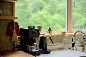 Una cocina con cafetera, hervidor y ventana con vistas a zonas verdes.
