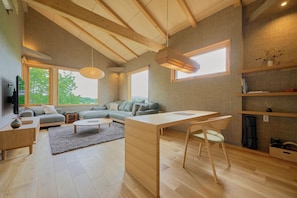 A spacious living area with a wooden ceiling, a sofa set, a dining table, and a fireplace. - Ume House (Kutchan)
