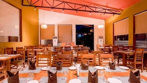 En restaurant med flere borde og stole, et loft med en spærkonstruktion, og udsigt til nattehimlen gennem vinduerne.