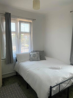 Ein Schlafzimmer mit einem Bett, einem Fenster mit Vorhängen, einem Heizkörper und einem gemusterten Teppich.
