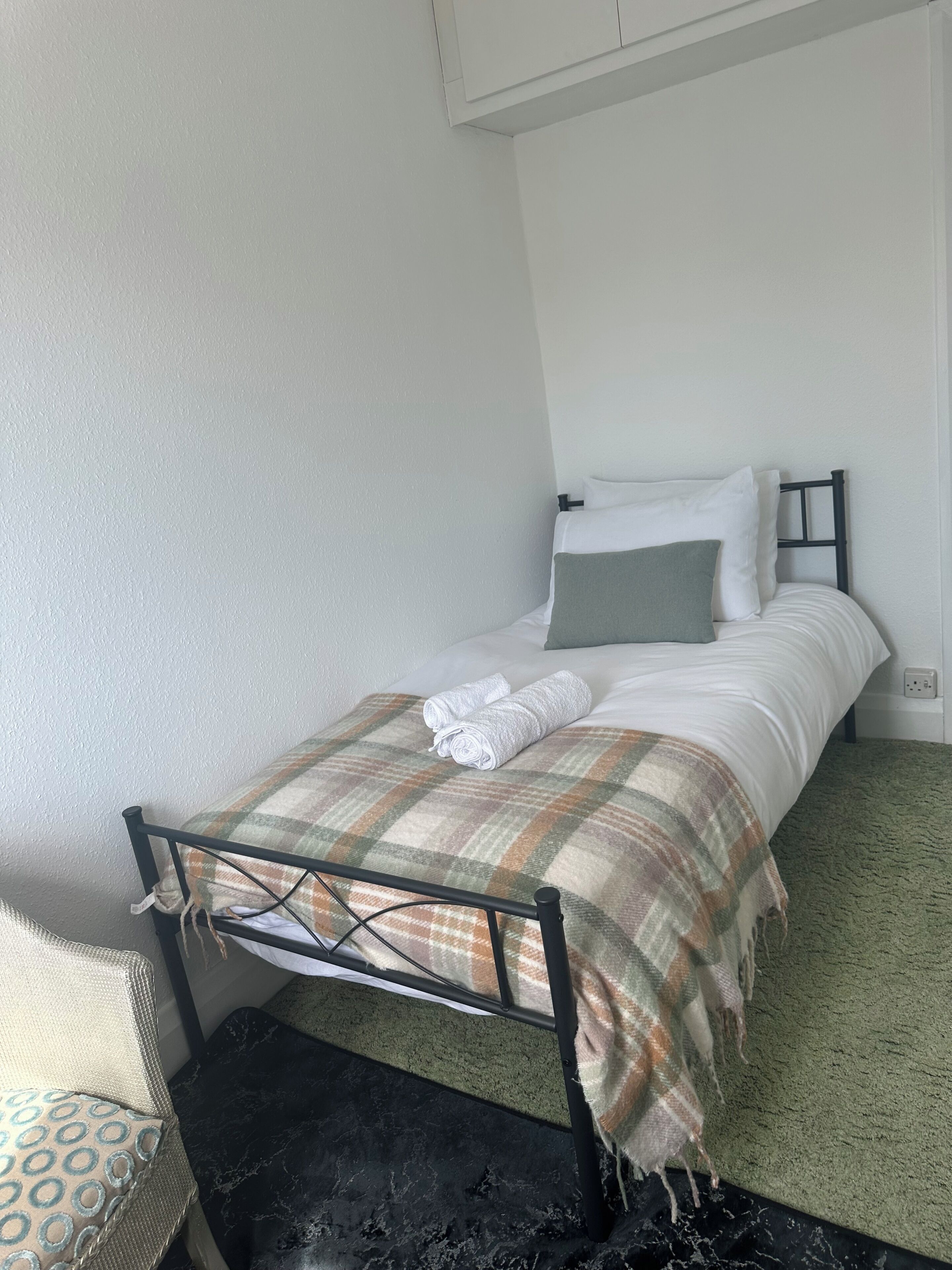 A single bed with a metal frame, white bedding, and a plaid blanket.