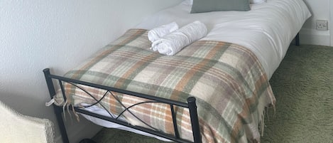 A single bed with a metal frame, white bedding, and a plaid blanket.