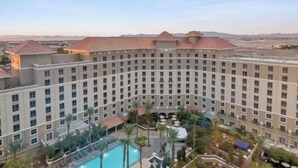 Een hotel met meerdere verdiepingen, een centrale binnenplaats, een zwembad en palmbomen.