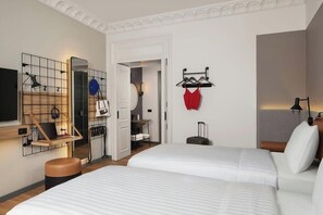 A hotel room with two beds, a desk with a laptop, a mirror, and a coat rack with clothes. - Moxy Istanbul Beyoglu (Istanbul)