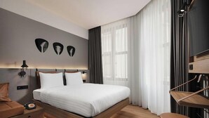 A modern hotel room with a large bed, a bedside table, a lamp, and a view of the outdoors. - Moxy Istanbul Beyoglu (Istanbul)