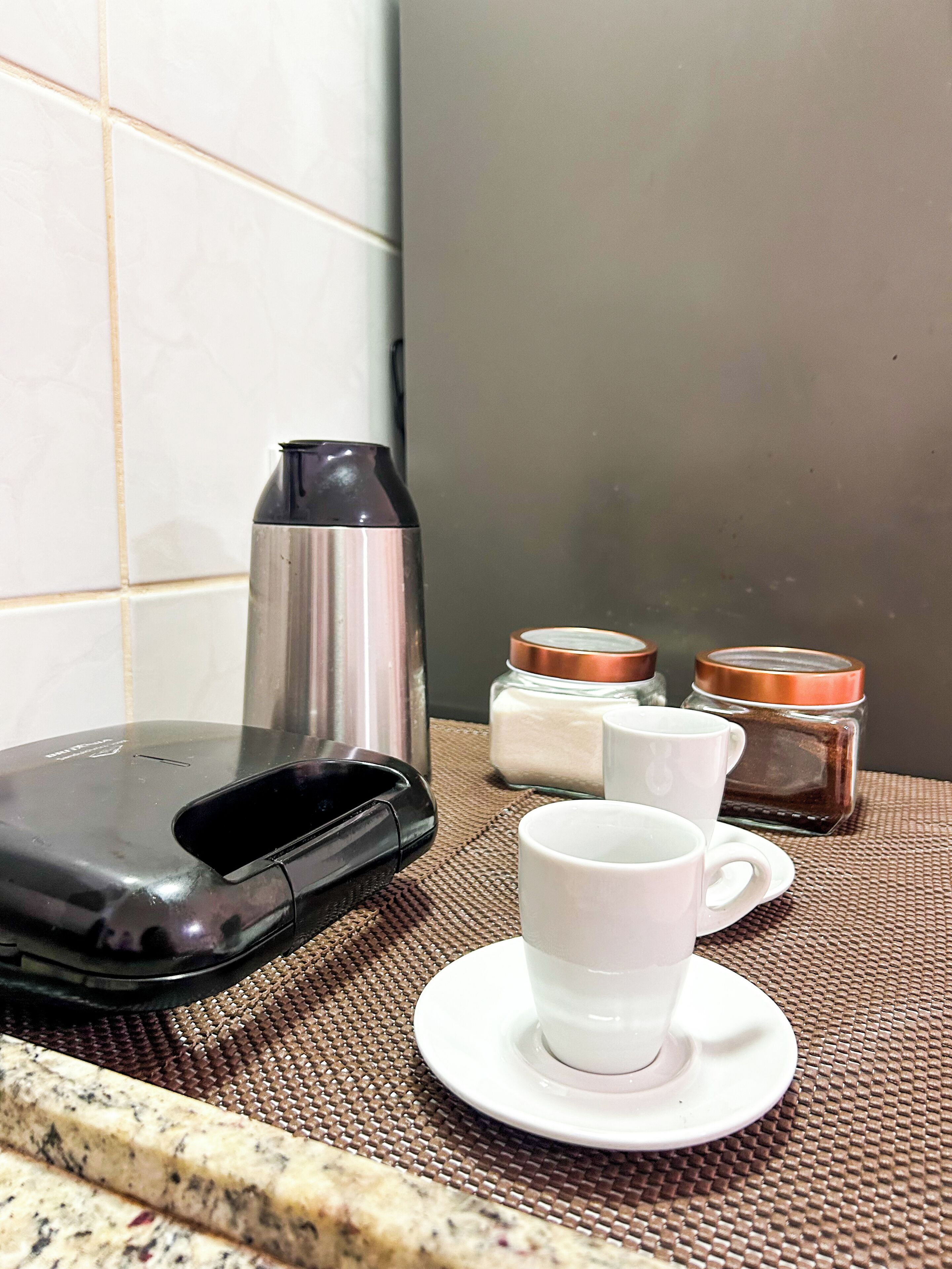 A kitchen area with a coffee maker, a white mug on a saucer, and two spice jars.